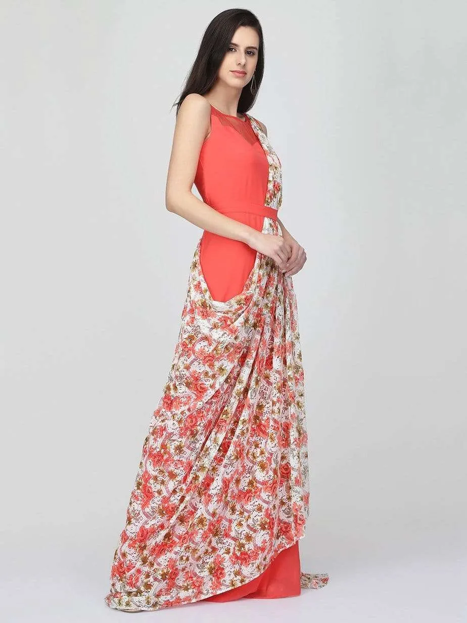 A woman in an Eavan Coral Drape Gown—sleeveless with a floral-patterned accent—poses sideways against a plain light background, one hand elegantly on her waist.